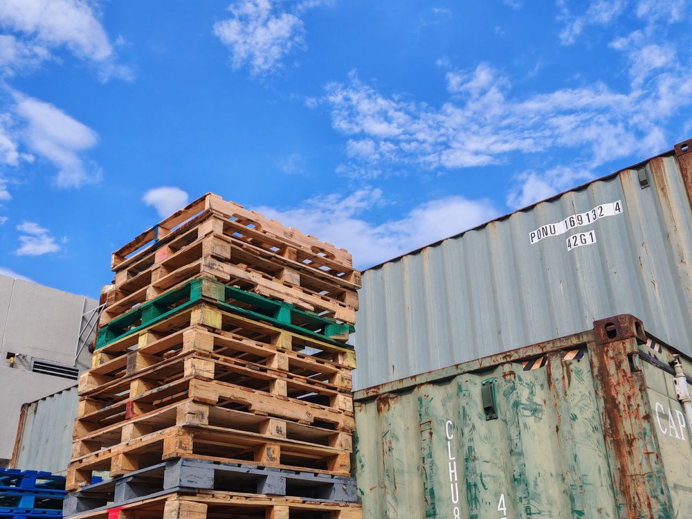 Pallets stacked beside shipping containers